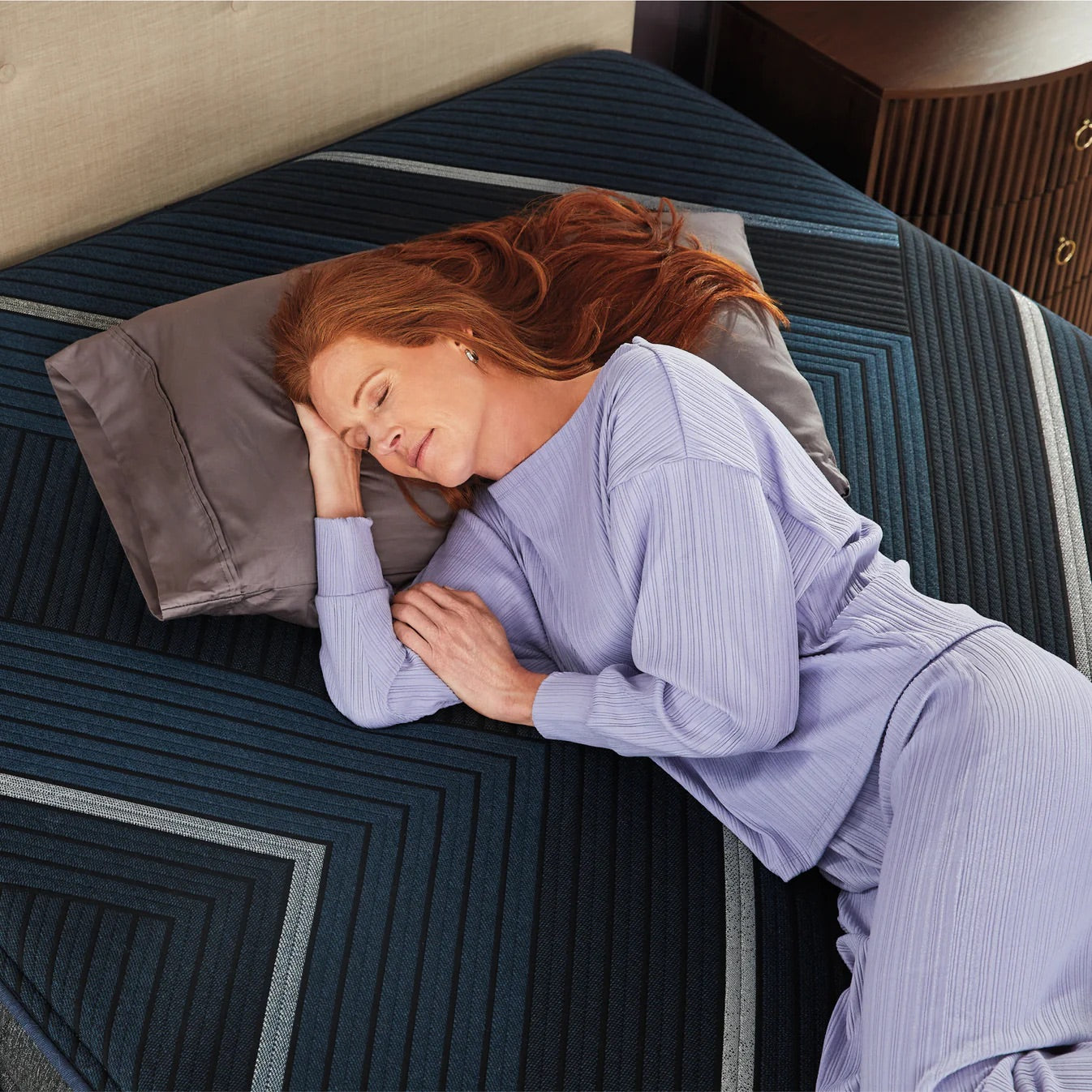 Woman in a purple outfit lying on a bed with a striped pattern