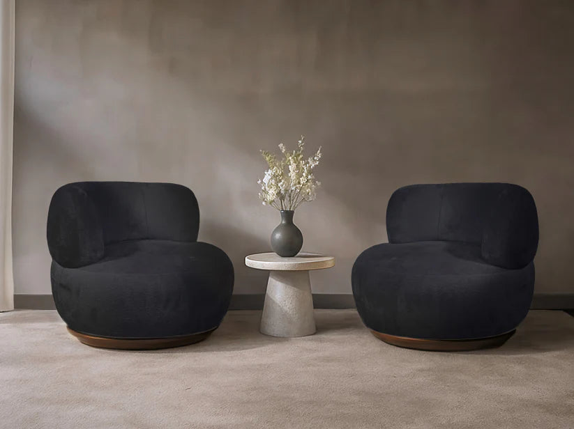 Two dark gray armchairs with a small round table and vase of flowers in a minimalistic room.