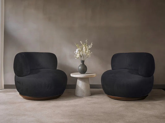 Two dark gray armchairs with a small round table and vase of flowers in a minimalistic room.
