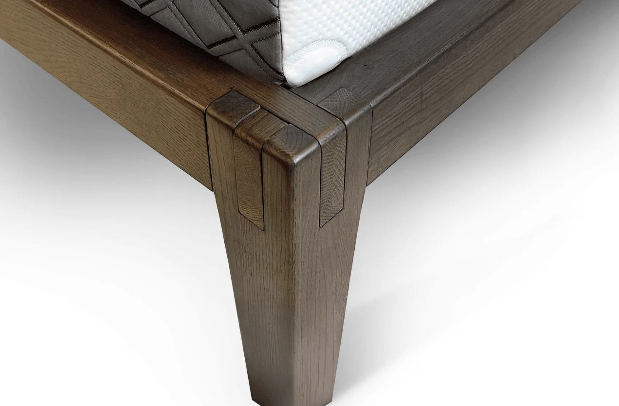 Close-up of a wooden bed frame with a white mattress on a light gray background