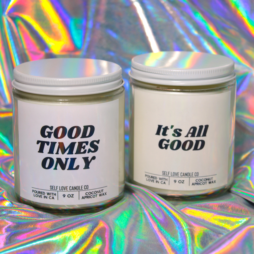 Two candles with 'Good Times Only' and 'It's All Good' text on a colorful, reflective background.