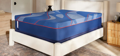 Blue mattress with red accents on a white bed frame in a bedroom setting.