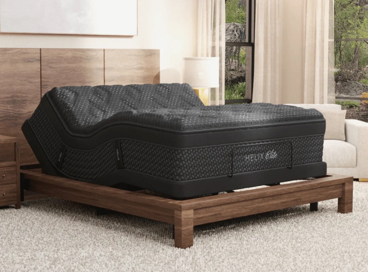 Helix elite mattress on adjustable base in a bedroom setting with wooden headboard and beige sofa.