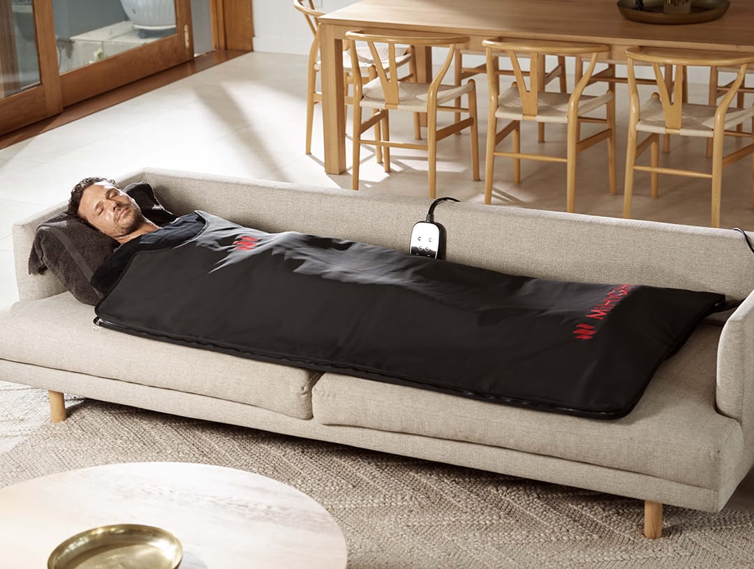 Person lying on a sofa in an infrared heated blanket, in a living room setting.