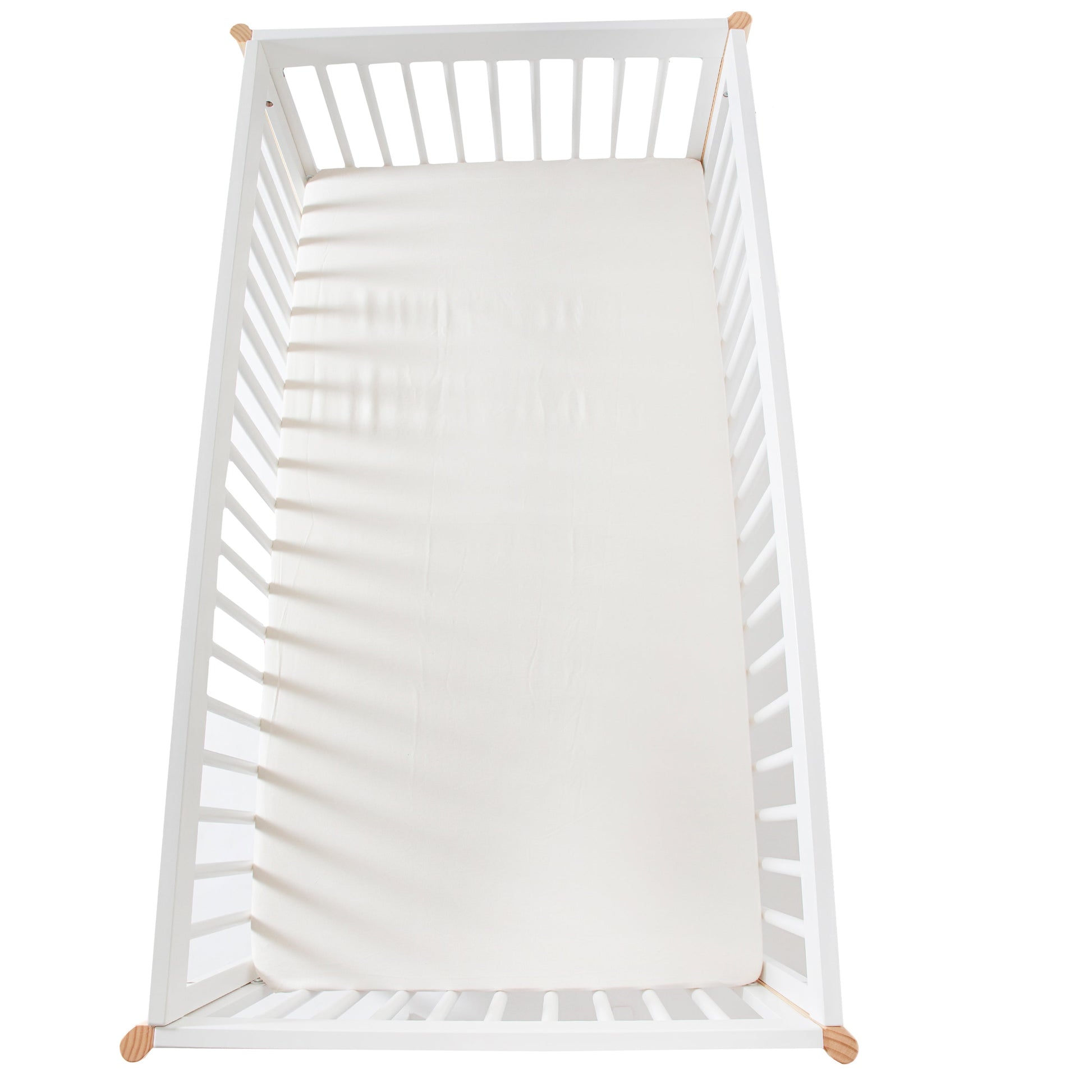 White crib with organic cotton sheets and wooden legs on a white background