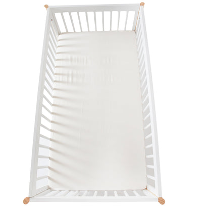 White crib with organic cotton sheets and wooden legs on a white background