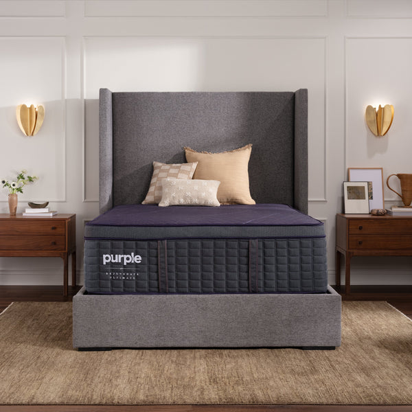Purple luxury mattress in a bedroom setting with gray headboard and wooden nightstands.