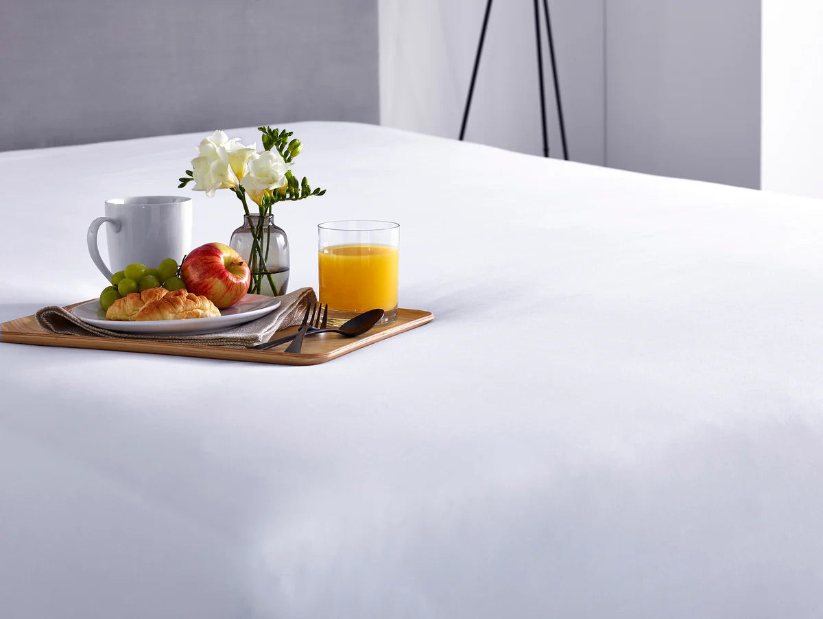 Breakfast tray with coffee, juice, and fruit on a white mattress protector