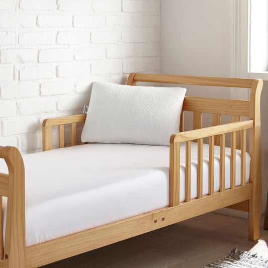 Wooden crib with white bedding against a white brick wall.