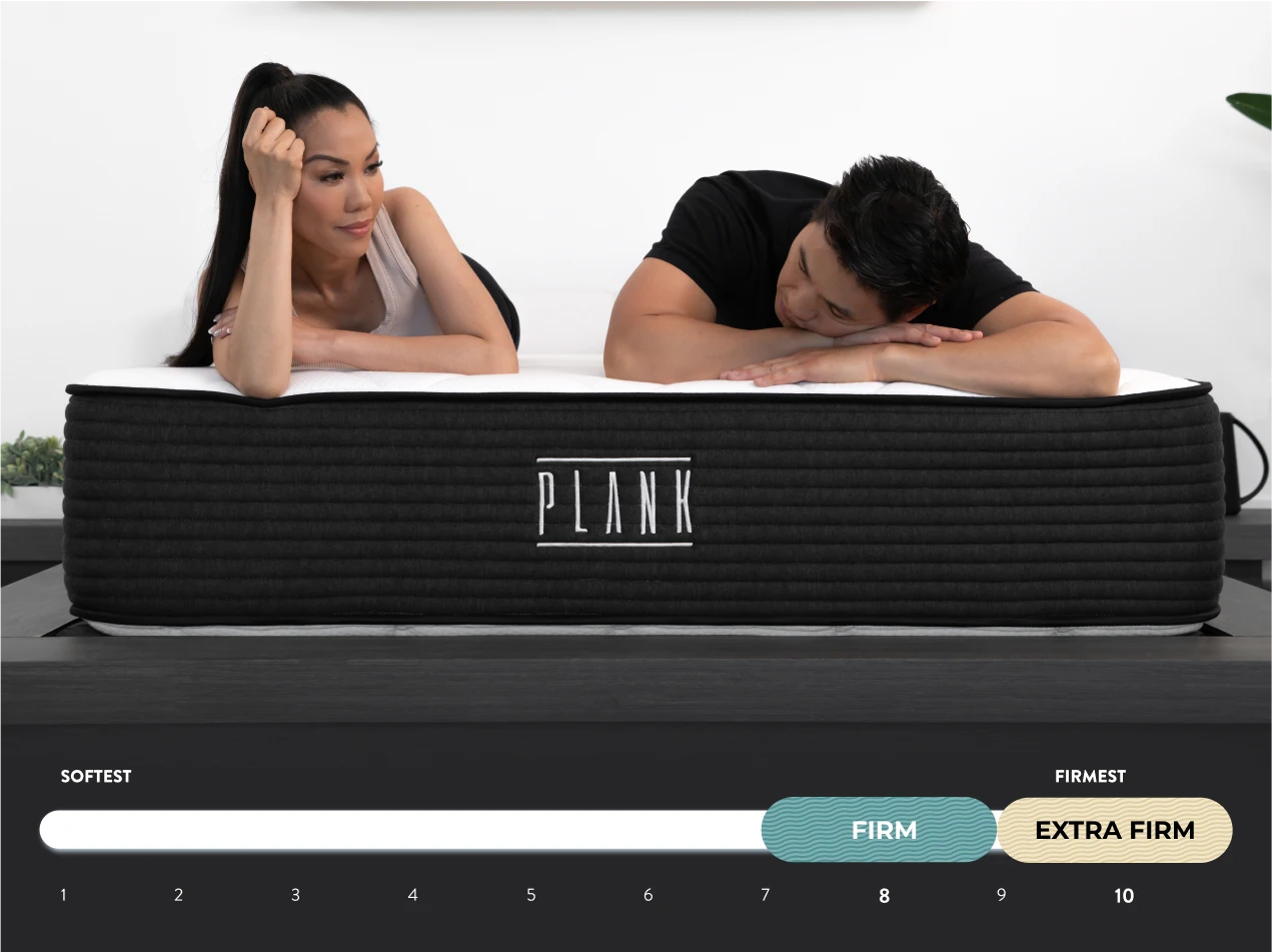 Two people lying on a PLANK mattress with a scale indicating firmness levels.