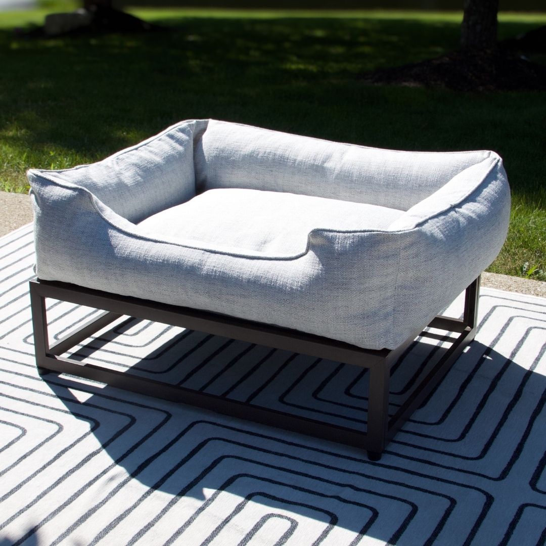 Dog bed on a metal frame outdoors on a patterned mat