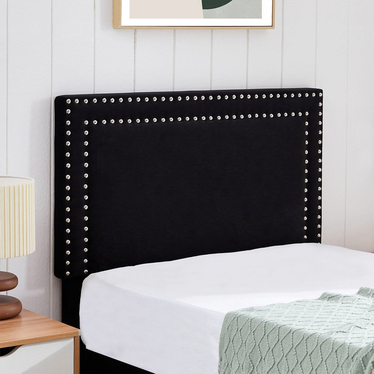 Black upholstered headboard with nailhead trim on a bed in a bedroom setting.