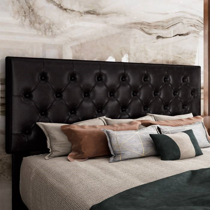 King size black bed with tufted black headboard and decorative pillows against a marble wall.