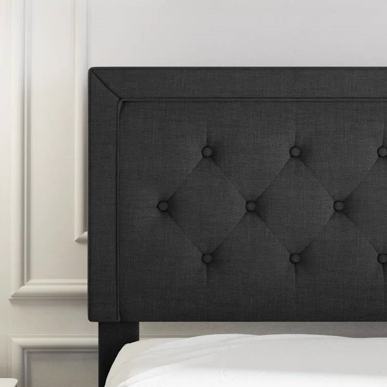 Full size black tufted headboard on a bed with white bedding against a light gray wall.
