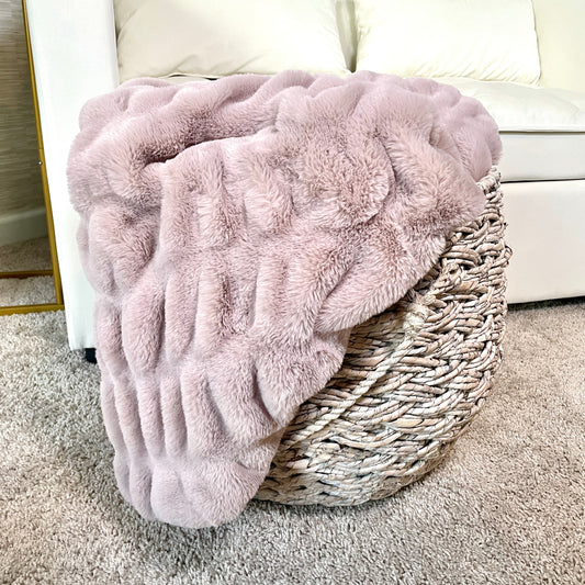 Pink fluffy blanket draped over a woven basket on a carpeted floor.