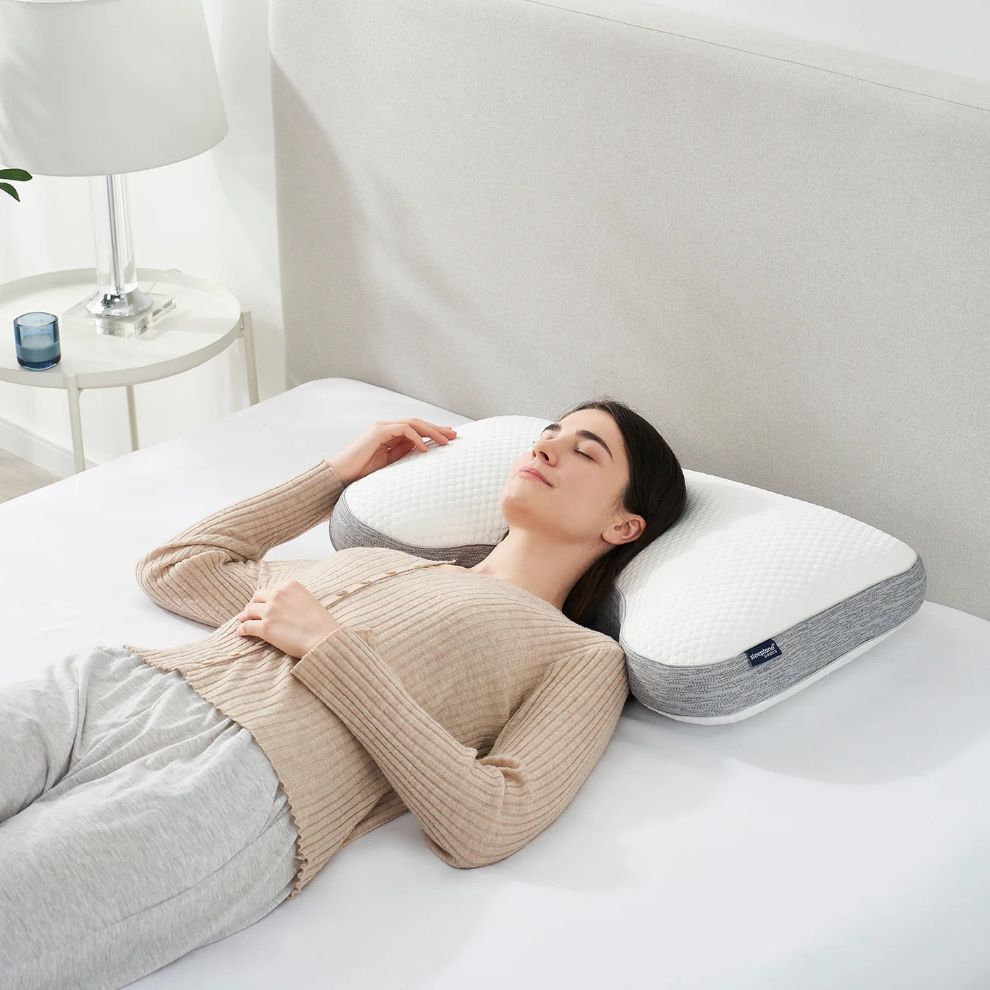 Woman lying on a bed with a cooling shoulder cutout pillow, in a bedroom setting.
