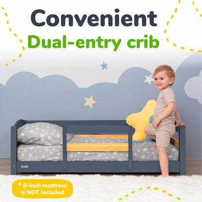 Child standing next to a convenient dual-entry crib with a blue wall and cloud design in the background.