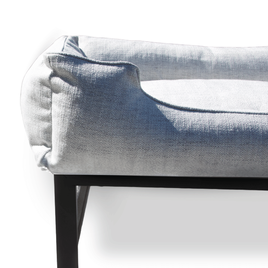 Gray upholstered dog bed on a black metal frame with a white background