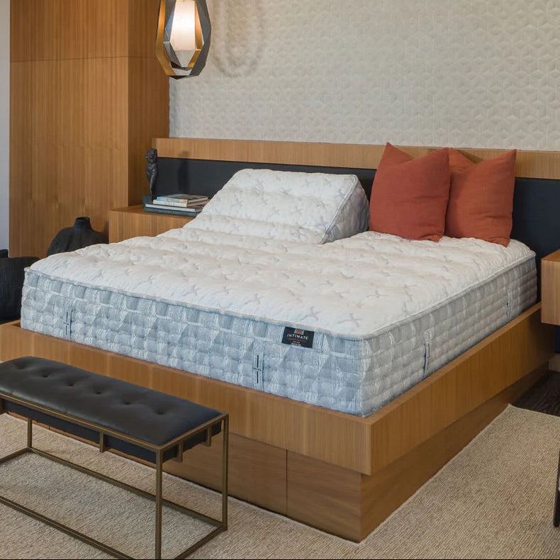 Bedroom with a mattress on a wooden bed frame, pillows, and a bench.
