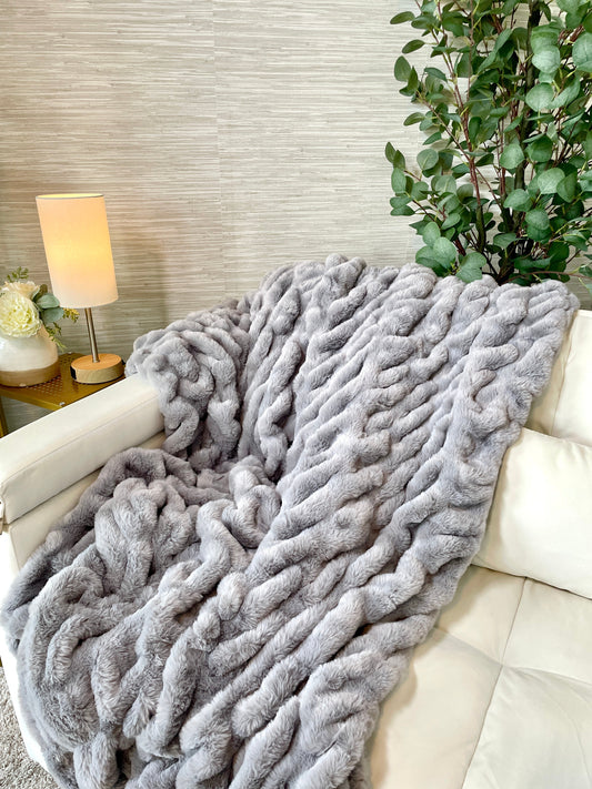 Gray fluffy blanket draped over a white sofa with a lamp and plant in the background.