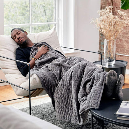 Man lying on a couch under a gray weighted blanket in a modern living room.
