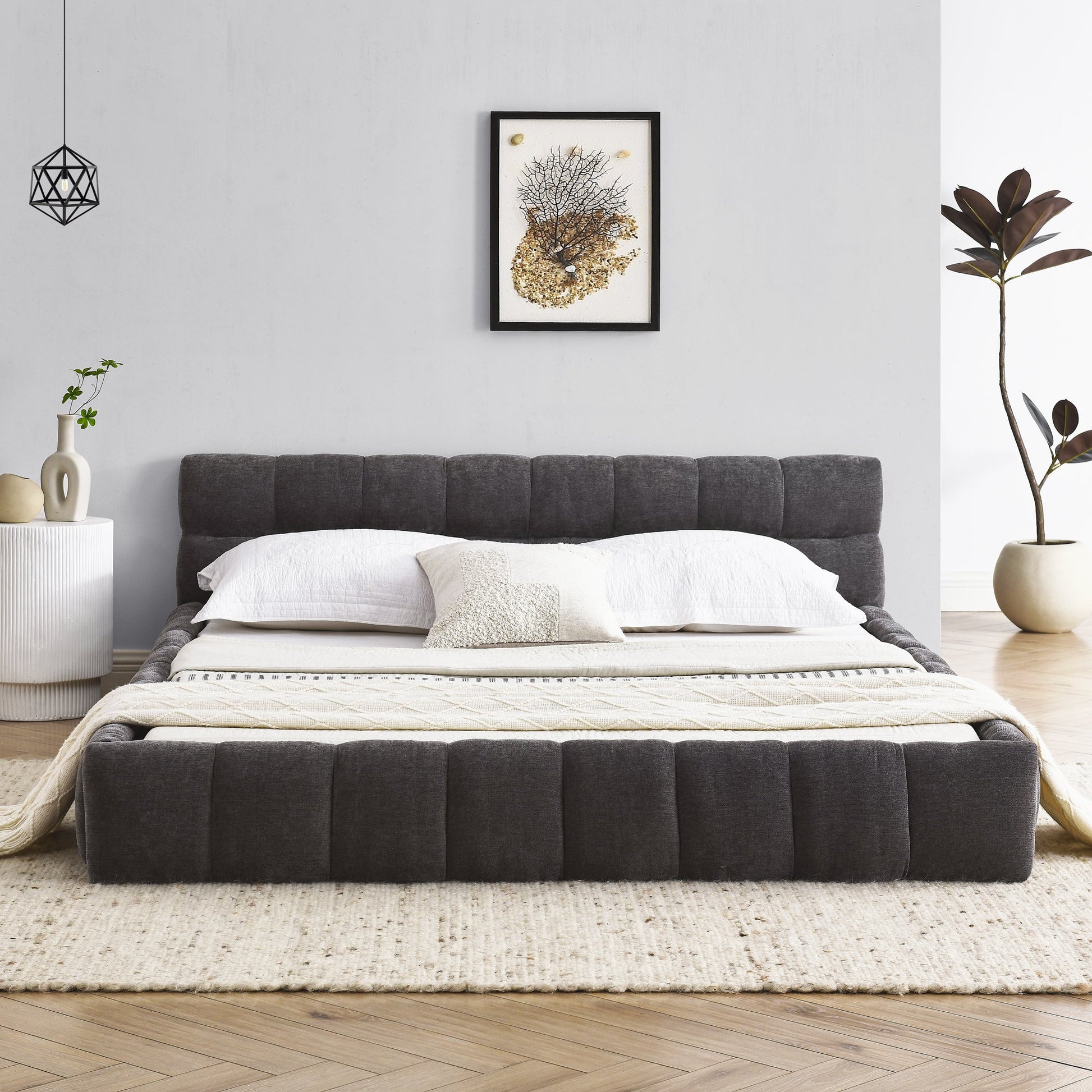 Gray queen upholstered bed in a modern bedroom with white walls, a side table, and decorative elements.