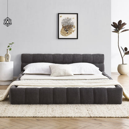 Gray queen upholstered bed in a modern bedroom with white walls, a side table, and decorative elements.