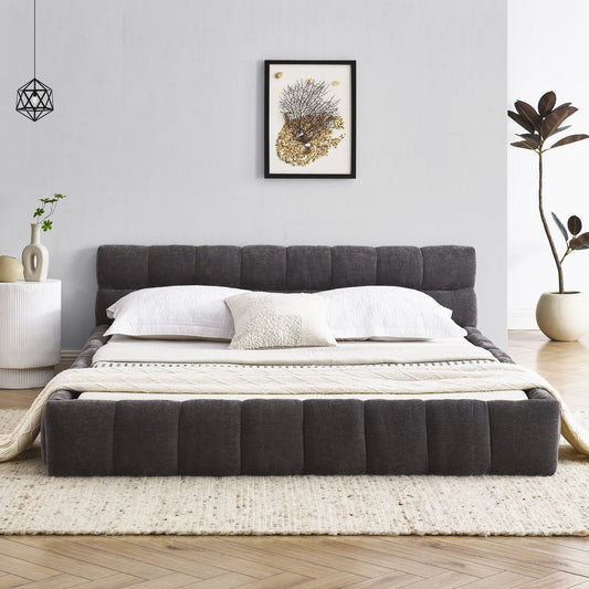 Gray queen upholstered bed in a modern bedroom with white walls, a side table, and decorative elements.