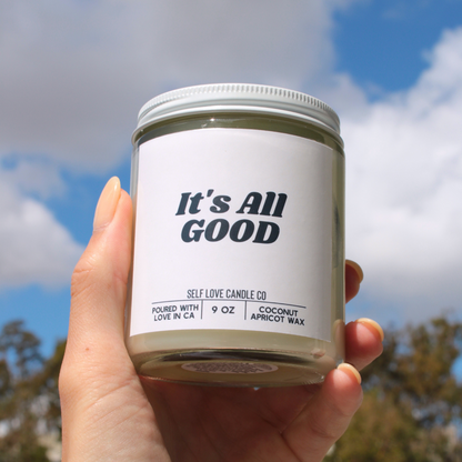 Hand holding a candle labeled 'It's All Good' against a blue sky background