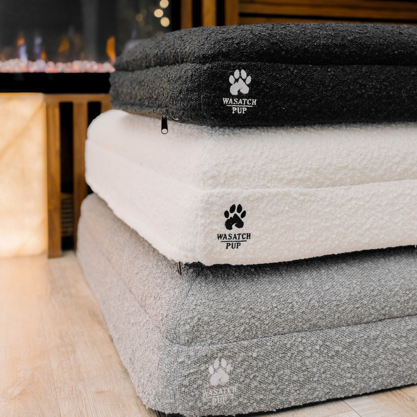 Stack of pet beds with 'Wasatch Pup' branding on a wooden floor.