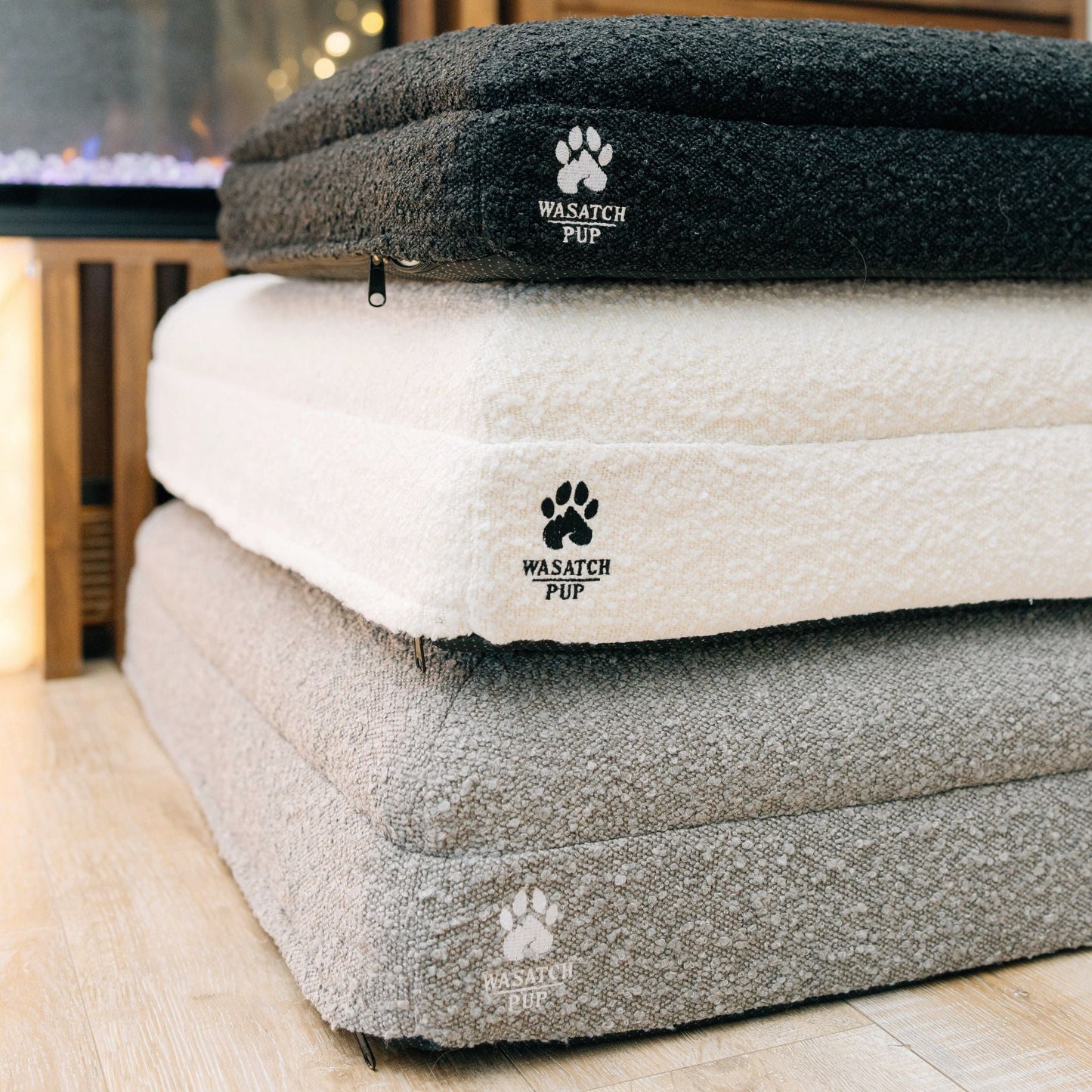 Stack of luxury pet beds with 'Wasatch Pup' branding on a wooden floor.