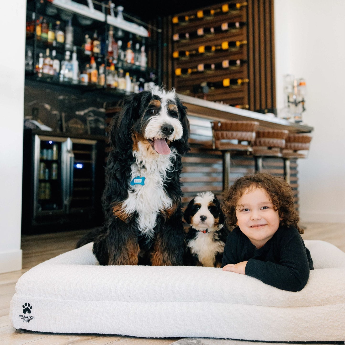 Child and two dogs on a large white pet bed in a modern interior setting.