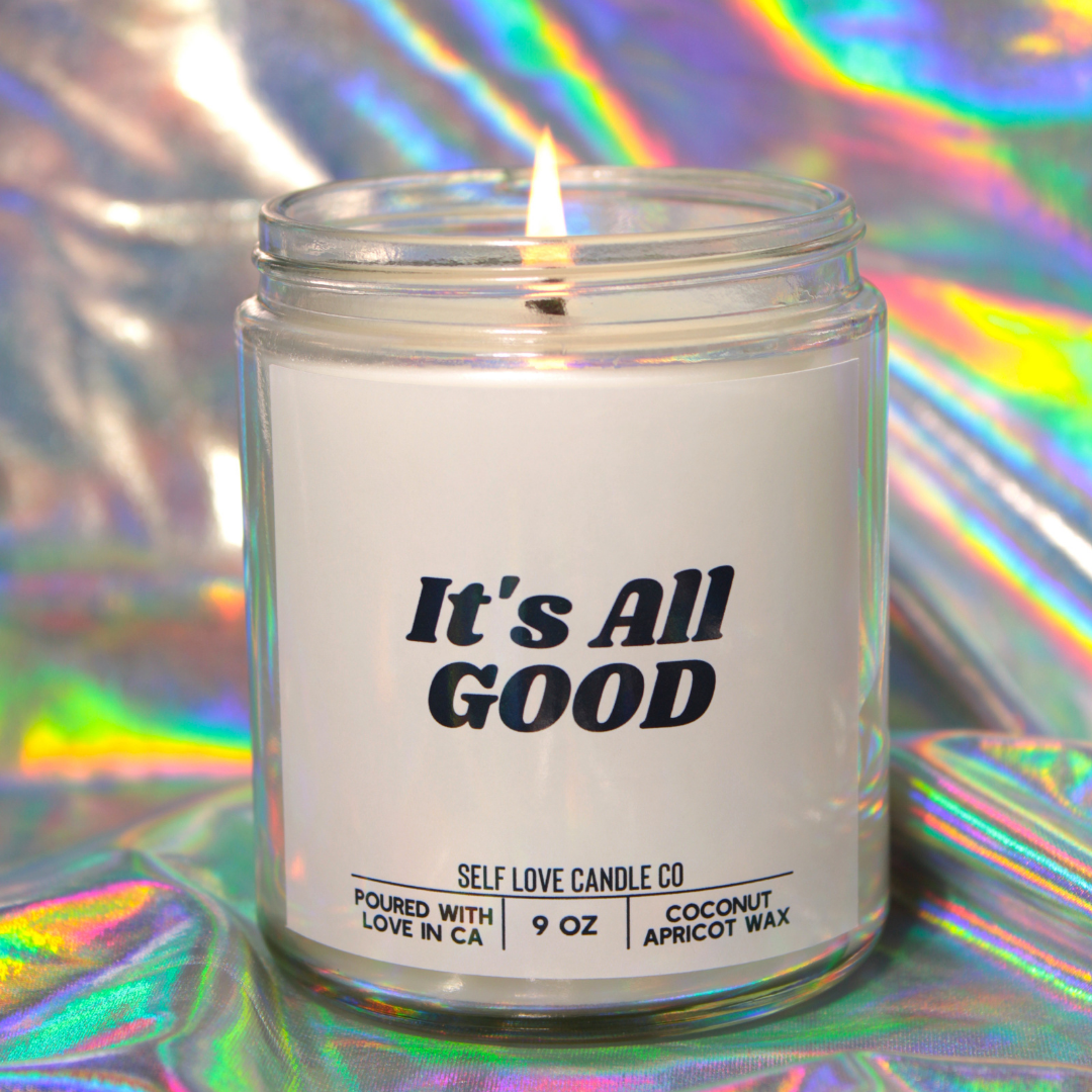 Candle in a clear jar with 'It's All Good' label on a colorful, reflective background