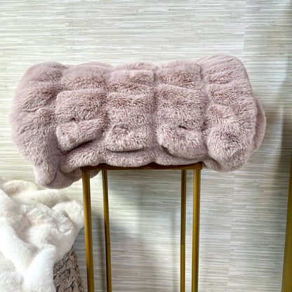 Pink fluffy blanket on a gold stool against a textured wall.