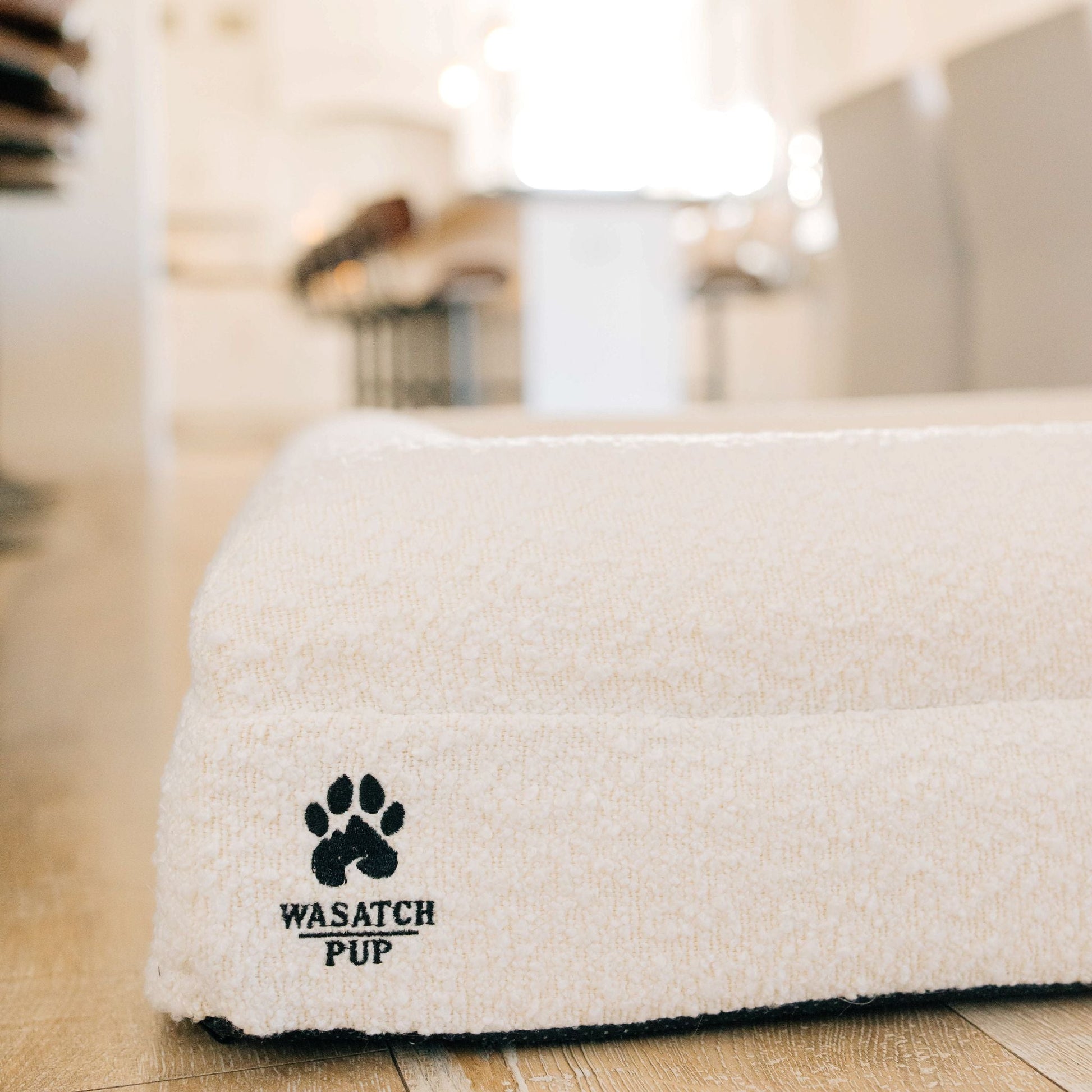 White washable pet bed with 'Wasatch Pup' logo on a wooden floor.