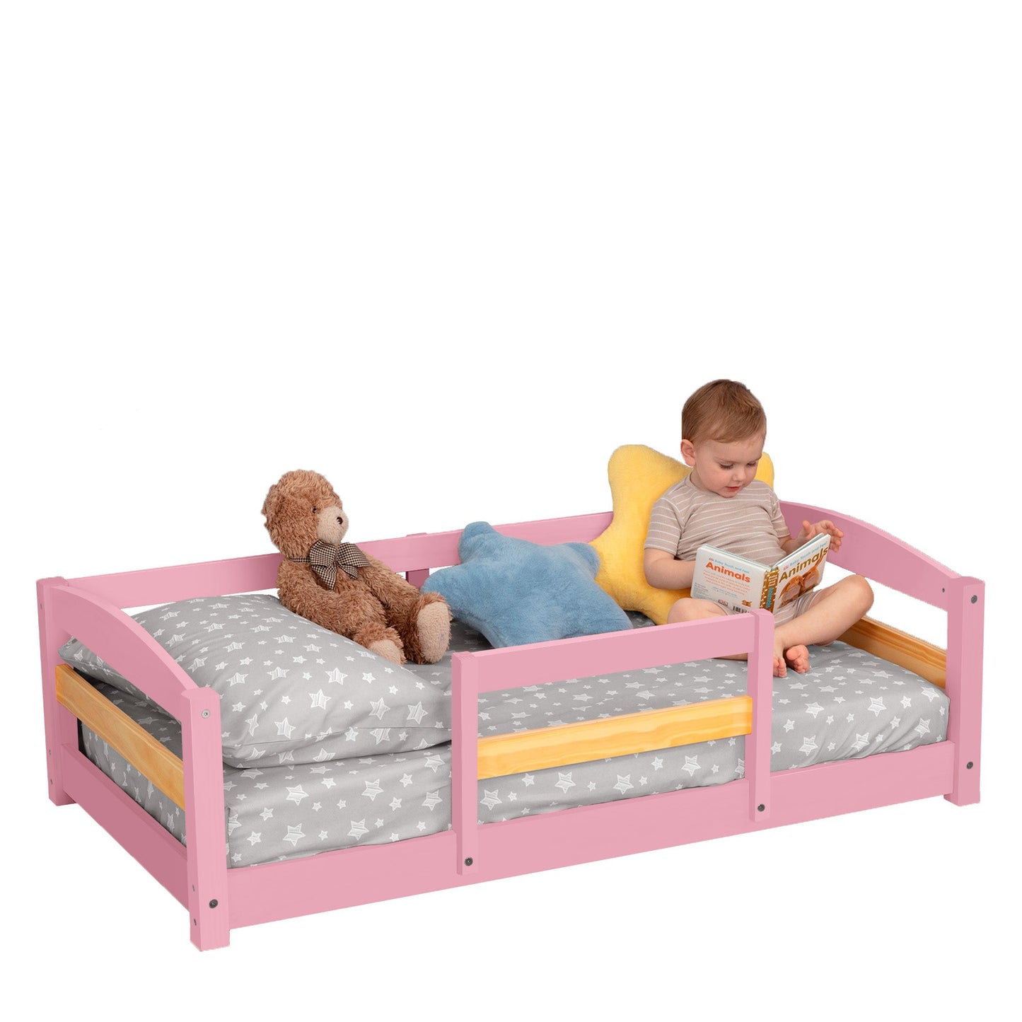 Child reading a book on a pink bed with toys and cushions.