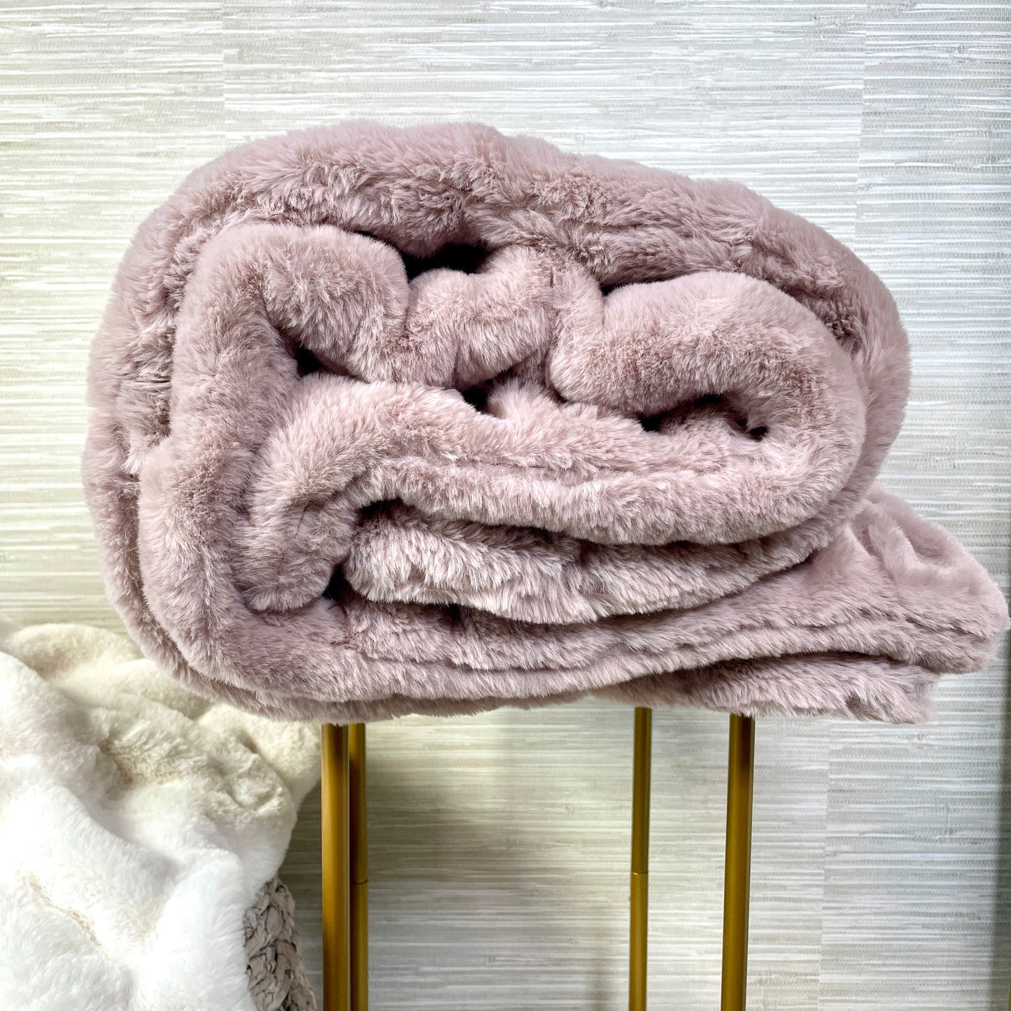 Pink plush blanket on a gold stool against a light background