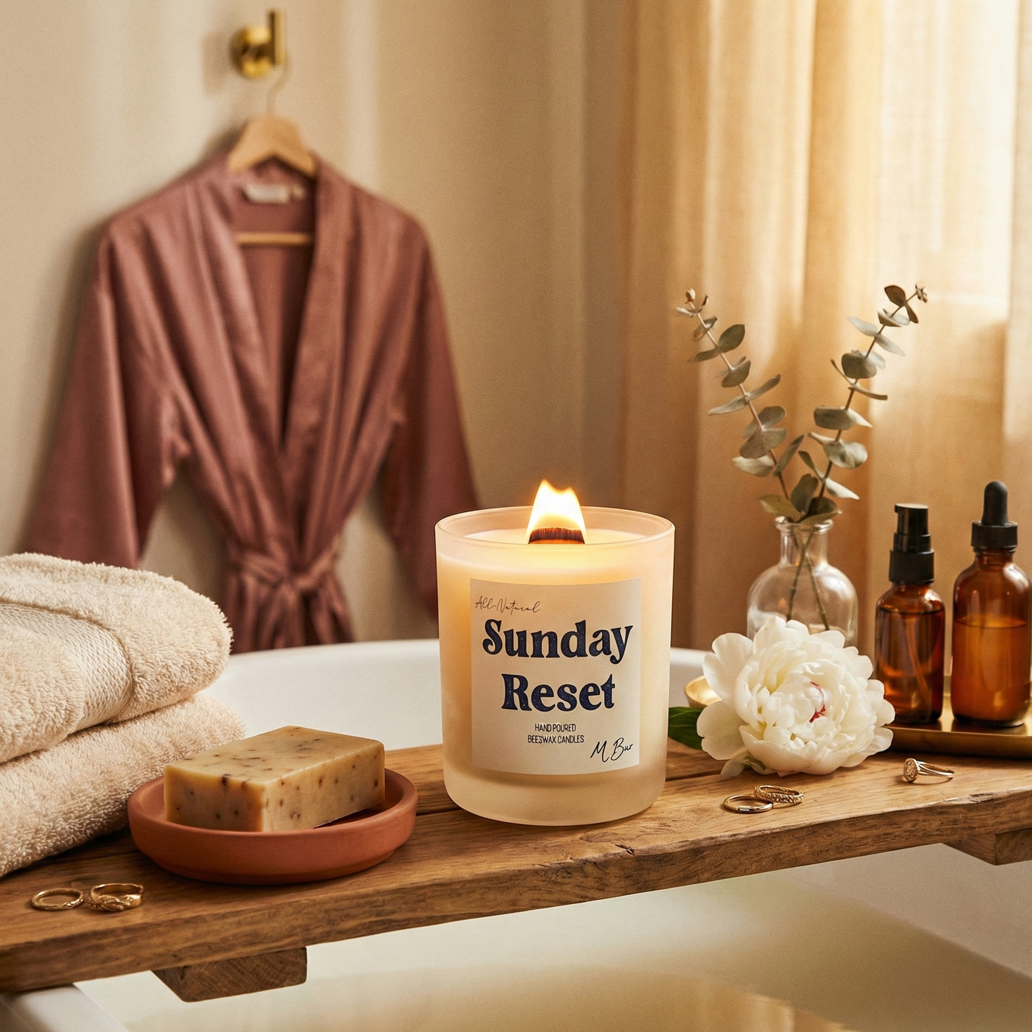 Candle labeled 'Sunday Reset' on a bathroom counter with bathrobes and toiletries in the background.