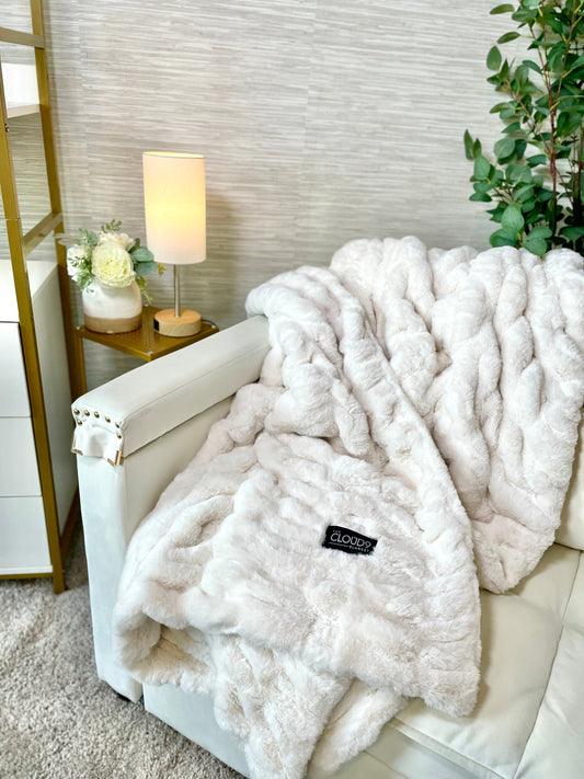 White fur throw blanket on a sofa with a lamp and plant in the background