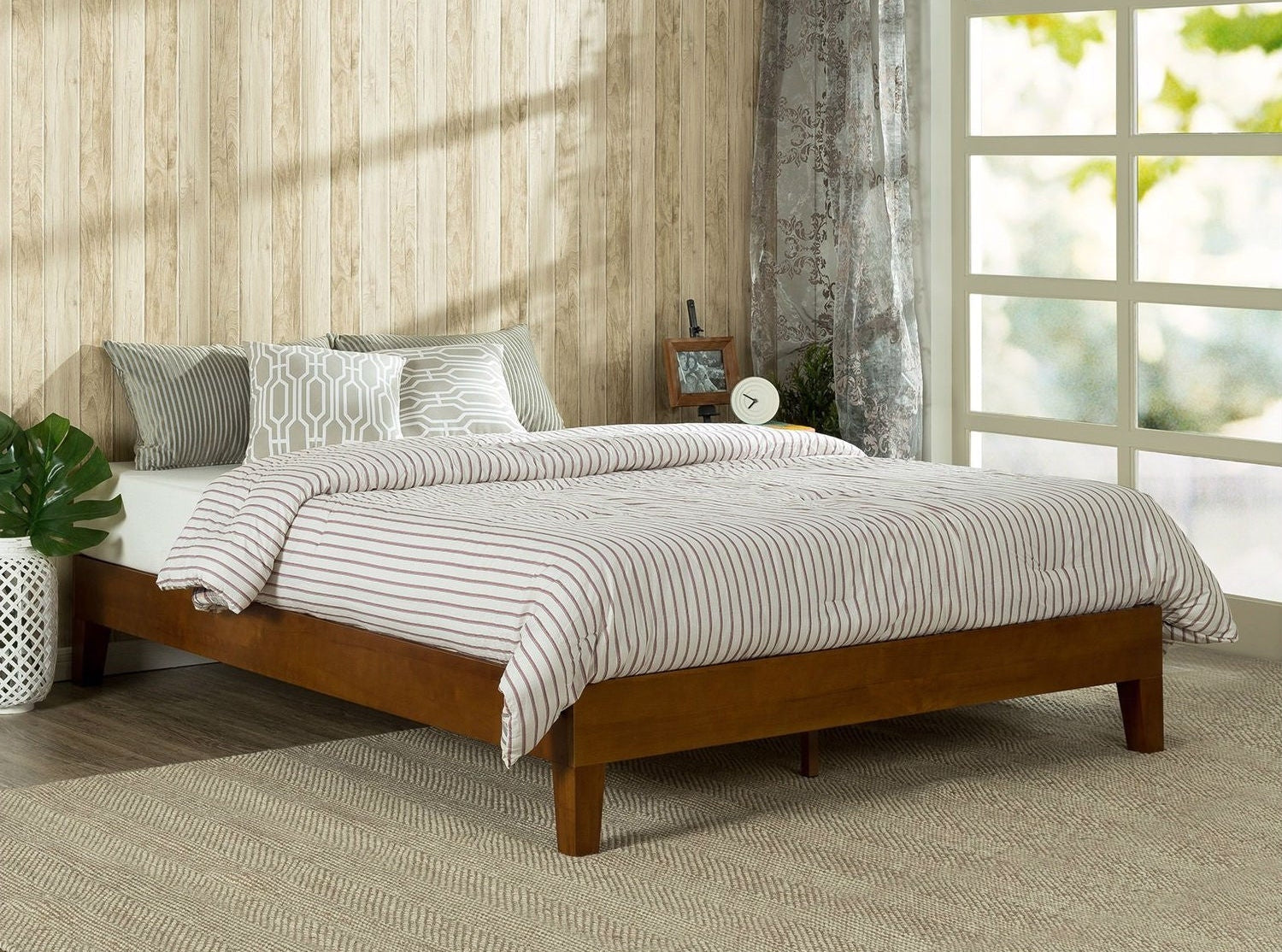 Wooden bed with striped bedding in a room with a window and plant